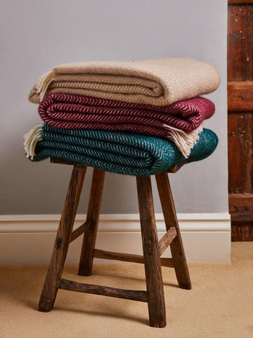 Stack of three folded dune pure new wool throws in beige maroon and teal with herringbone weave and fringed edges