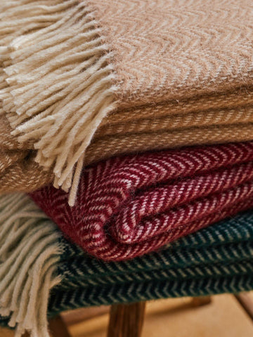 Stack of dune pure new wool throws in beige red and green with cream-colored fringe showing woven texture