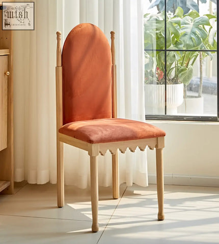 A warm orange ealing high-back velvet dining chair with light wood frame and scalloped base