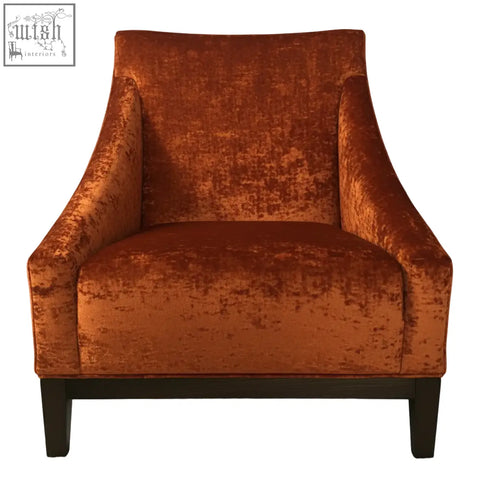 A plush burnt orange velvet ease arm chair with a high back and dark wooden legs for cozy seating