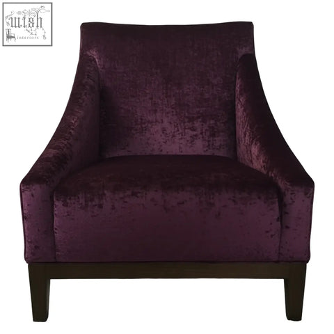 A plush deep purple velvet ease arm chair with tufted back and dark wooden legs perfect for cozy seating