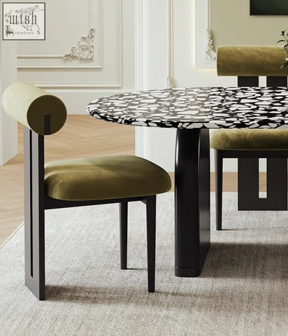 Olive green velvet chair with cylindrical backrest and black metal frame paired with eaton dining table terrazzo top