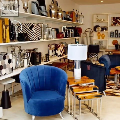 A plush royal blue velvet armchair with a curved back paired with an eben marble base table lamp with ivory shade