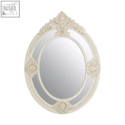 An ornate oval eclipse antique white mirror with a distressed frame and intricate floral scrollwork design