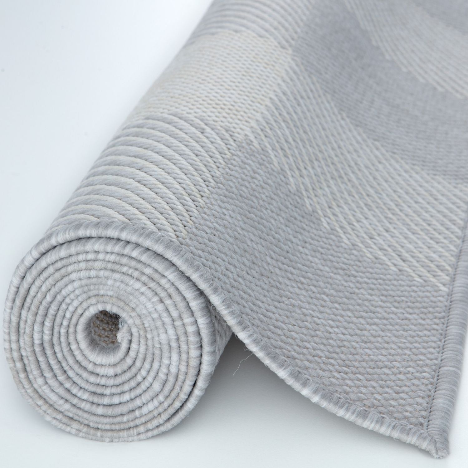 A neatly rolled ecology outdoor rug grey with a textured woven ribbed pattern and fringe along the edge
