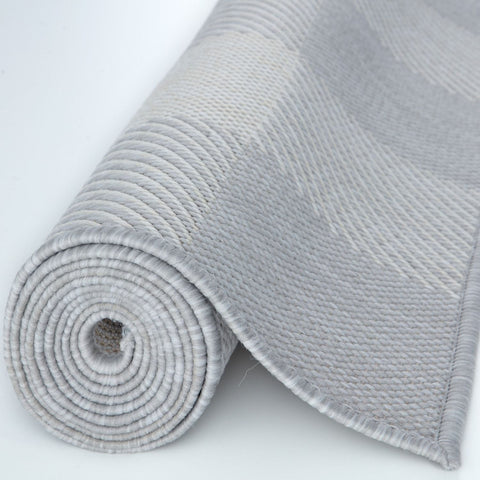 A neatly rolled ecology outdoor rug grey with a textured woven ribbed pattern and fringe along the edge