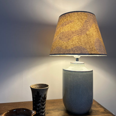A warm ecru wiggle empire lampshade with textured fabric on a matte gray ceramic table lamp base from the wiggle collection