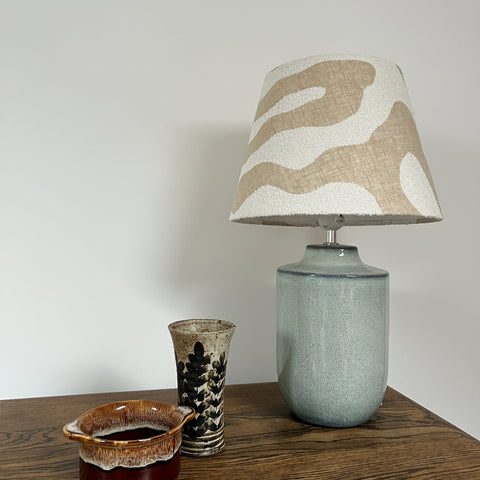 A ceramic table lamp with a matte sage green base and an ecru wiggle empire lampshade from the wiggle collection