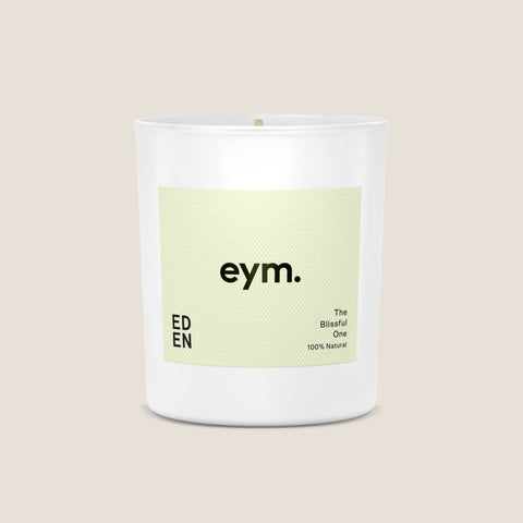 A minimalist white glass standard candle jar with a pale green eym label the blissful one 100 percent natural