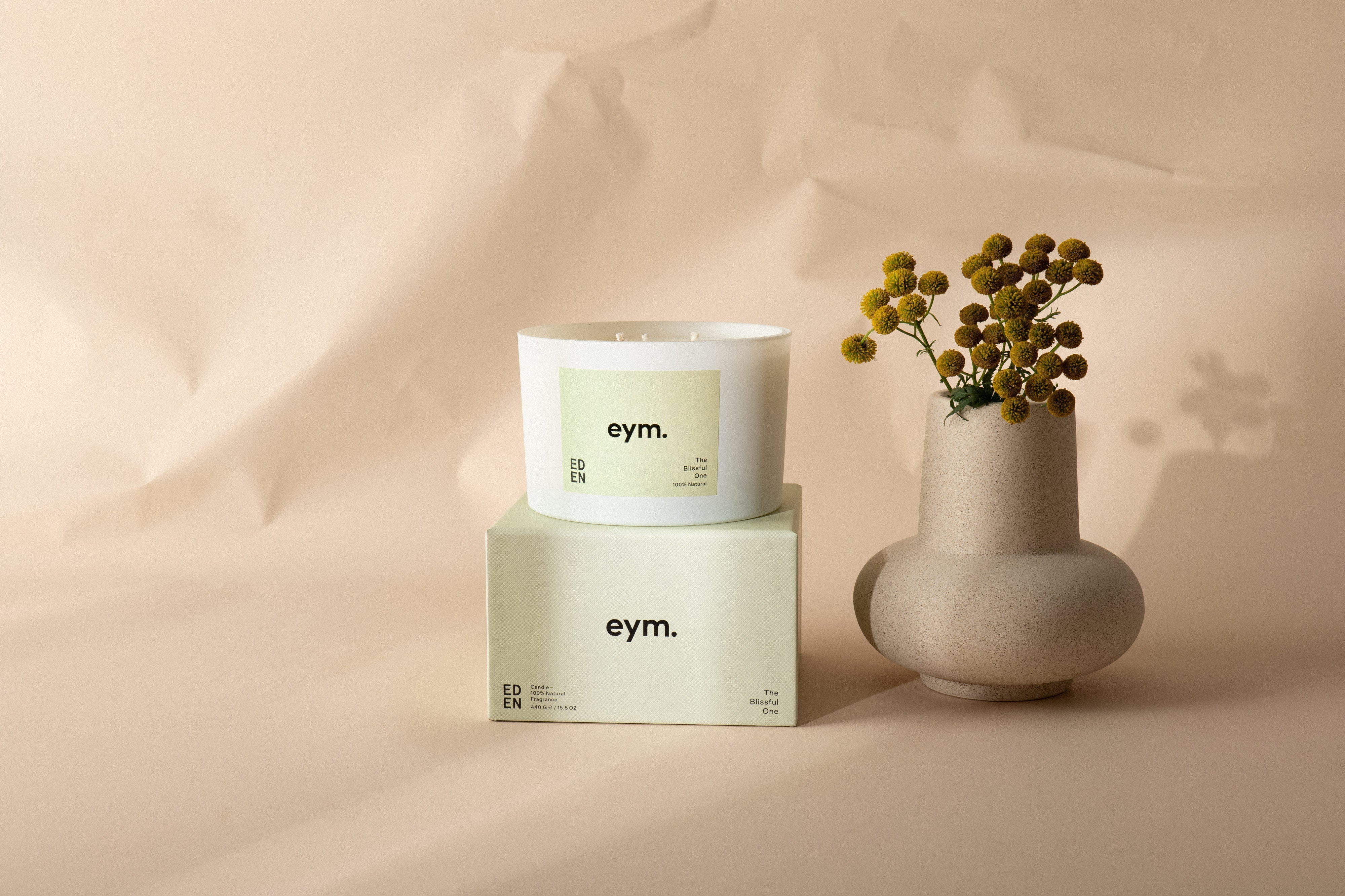 White cylindrical three wick candle with pale green eym label and matching branded box from eden collection