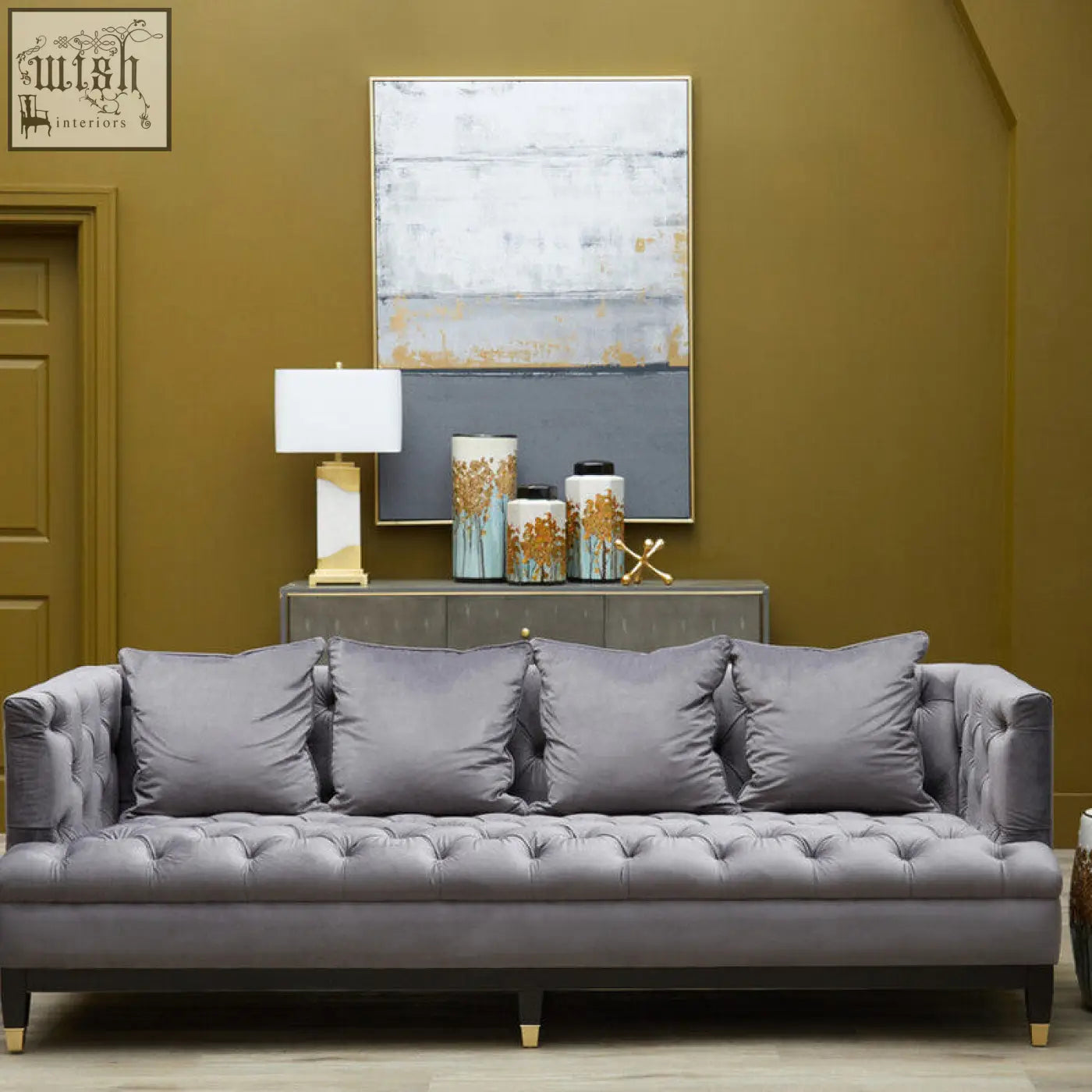 Gray tufted velvet sofa with dark wood legs and gold feet next to edith table lamp with white marble base and gold accents
