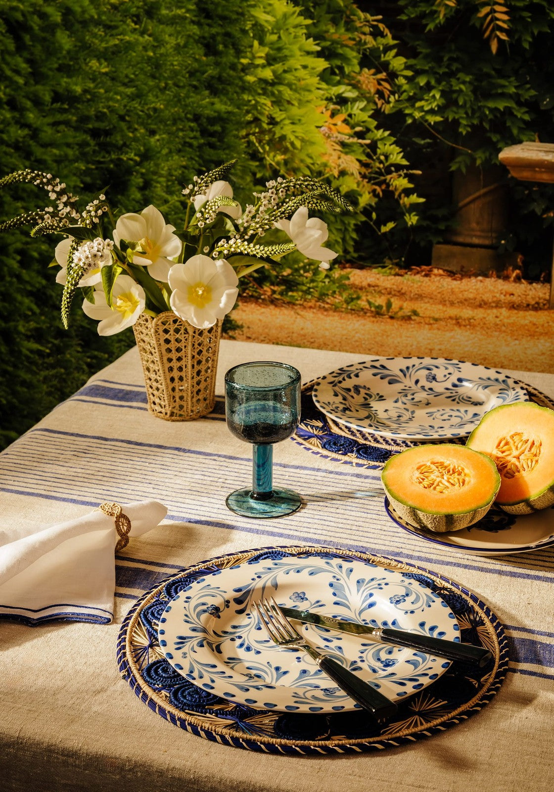 Blue and white ceramic plates with floral patterns on striped tablecloth shown with eleanor wine glass blue product