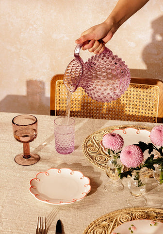 A translucent pink glass pitcher with a textured bubble surface and curved handle from eleanor wine glass violet collection