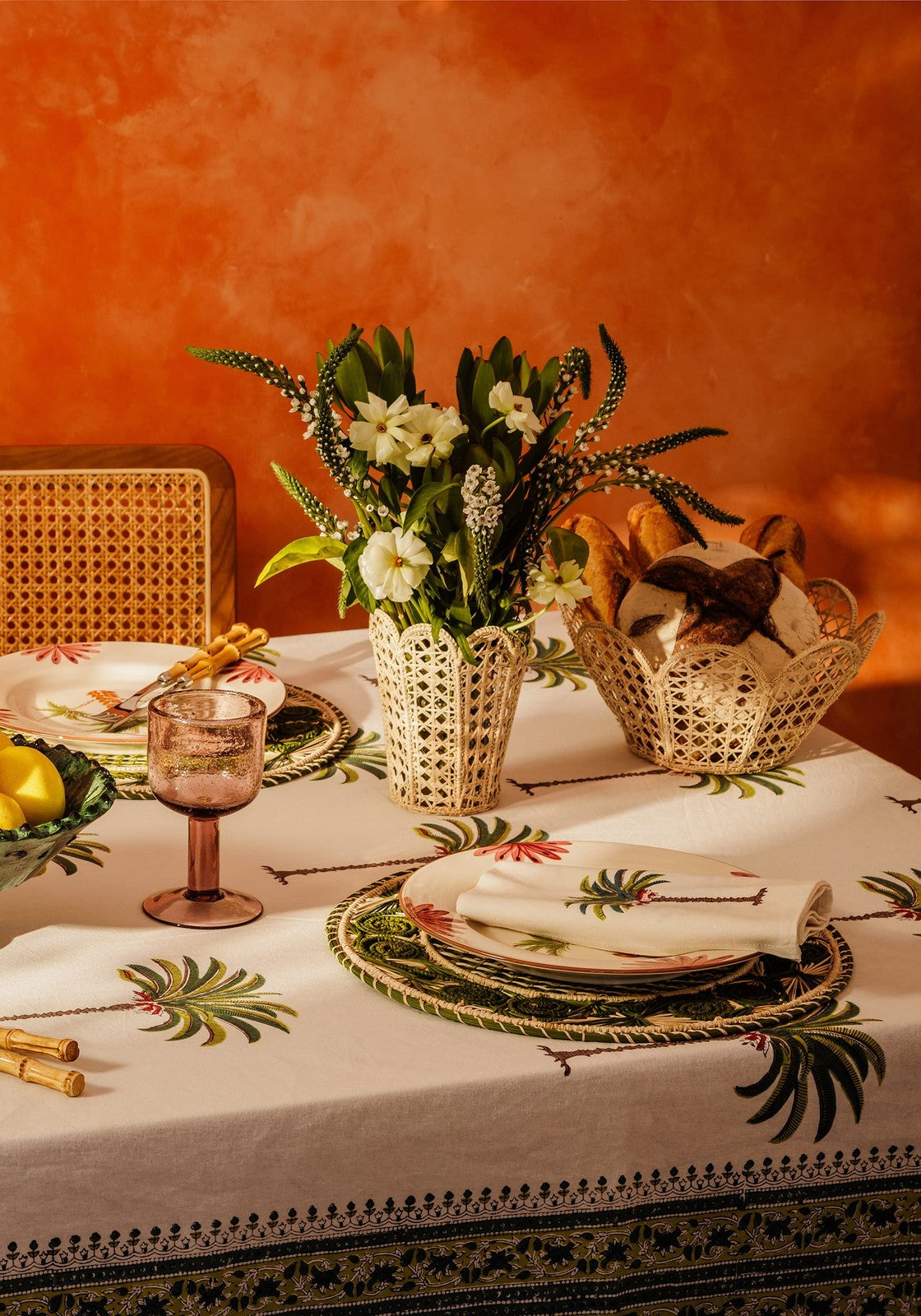 A white tablecloth with tropical palm leaf pattern and black embroidered border perfect for elegant dining
