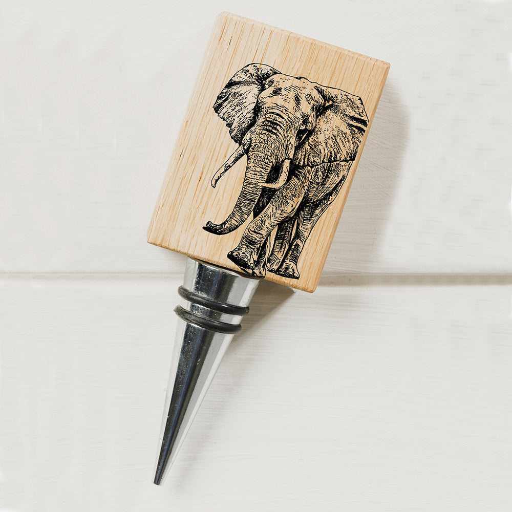 A wooden oak bottle stopper with a black engraved elephant on its square top and a metallic tapered stem
