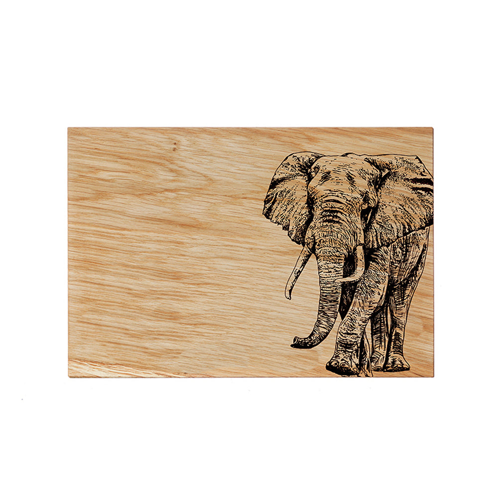 A rectangular light brown oak serving board with a detailed black-burned elephant design for cheese and snacks