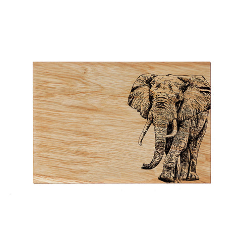 A rectangular light brown oak serving board with a detailed black-burned elephant design for cheese and snacks