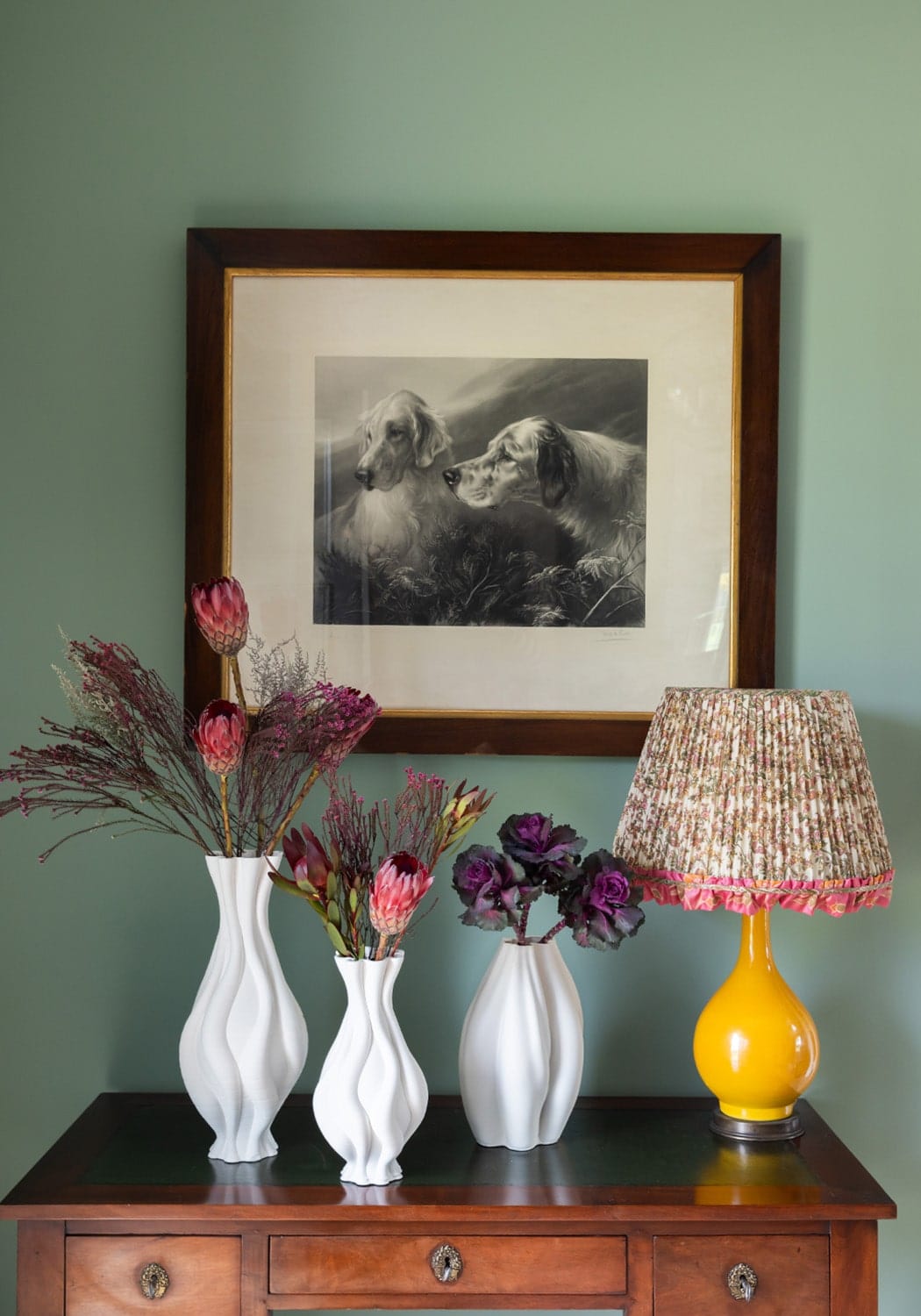 Three tall white ceramic vases with twisted wavy designs holding dried flowers and proteas