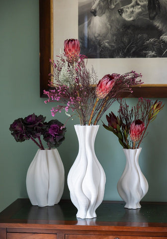 Three tall white ceramic vases with twisted wavy surfaces on a wooden surface perfect for home decor
