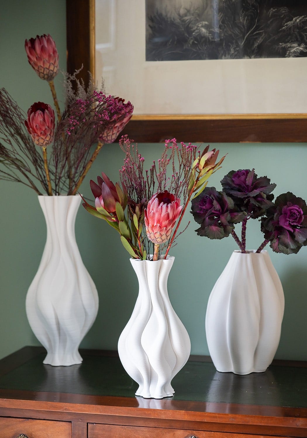 Three elegant white twisted ceramic vases with wavy surfaces holding vibrant dried flowers