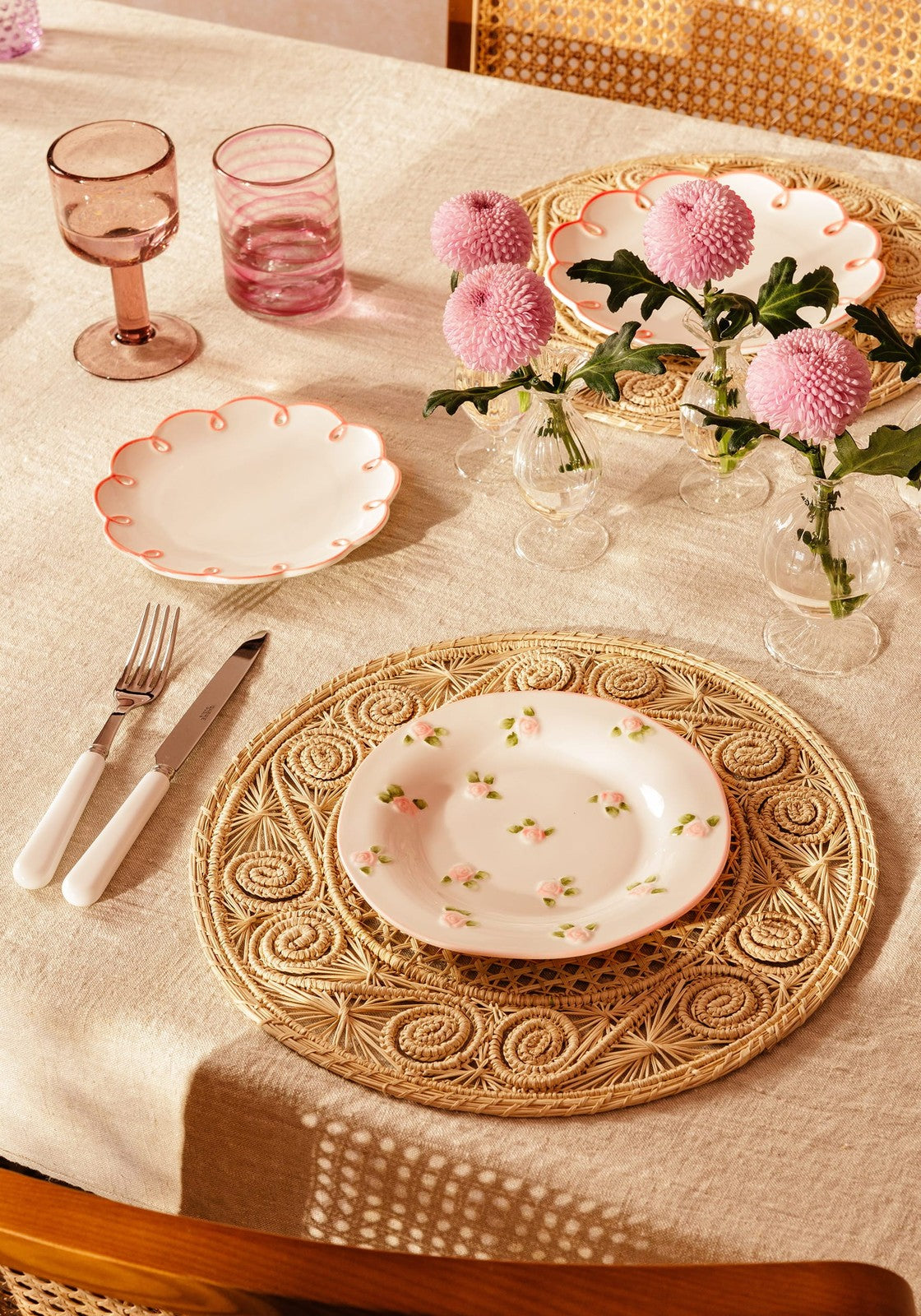 A delicate white ceramic plate with pink flowers on an oatmeal emma linen tablecloth over a rattan placemat