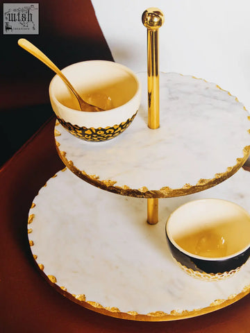 Gold finish cake stand with white marble tiers and black and white patterned bowls for elegant serving