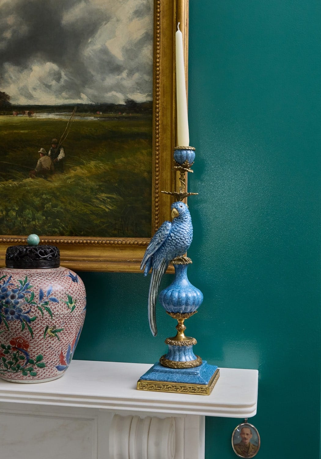 A blue enamelled ceramic pretty polly parrot candlestick with gold accents holding a white taper candle