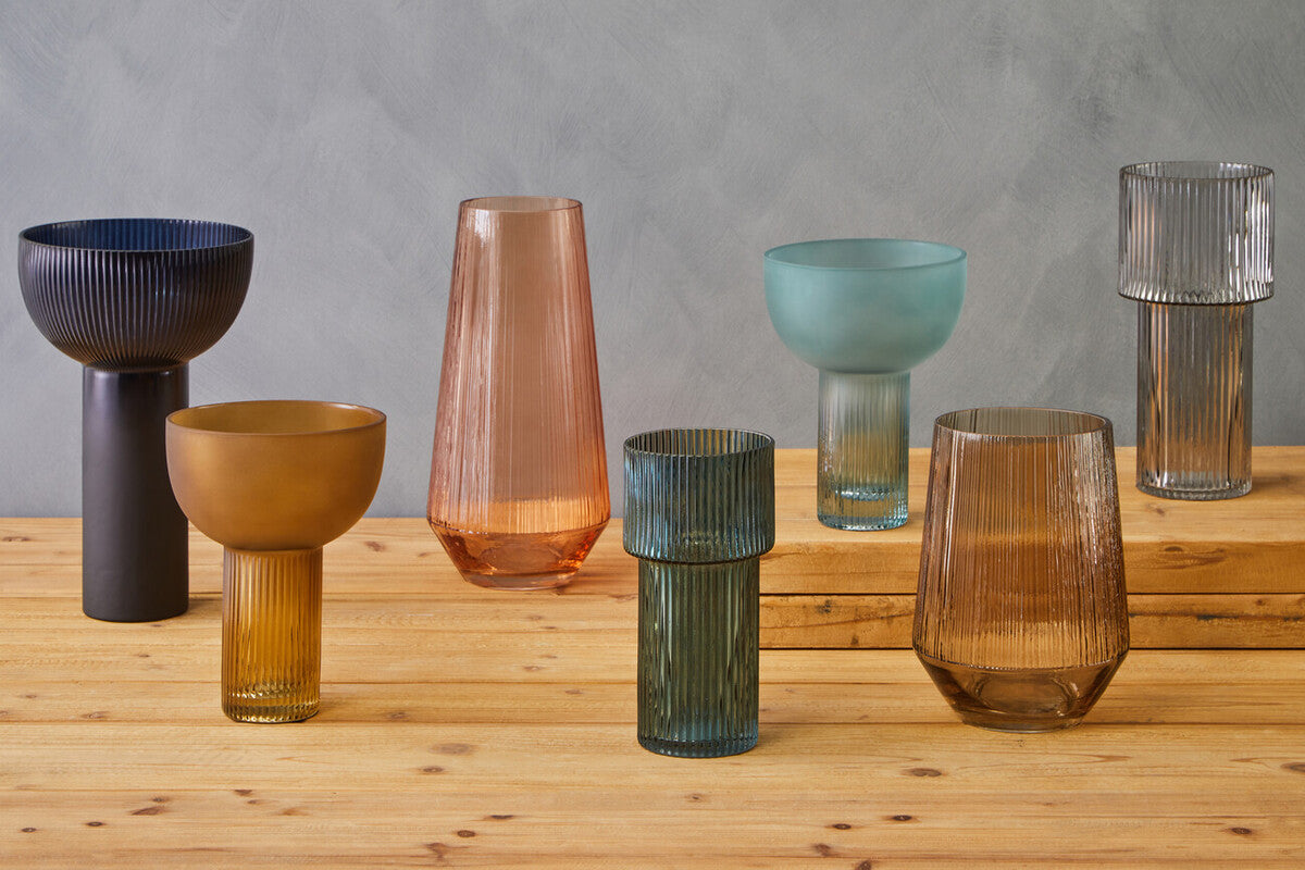 A collection of modern ribbed glass vases featuring the small light blue glass vase among earthy and pastel hues