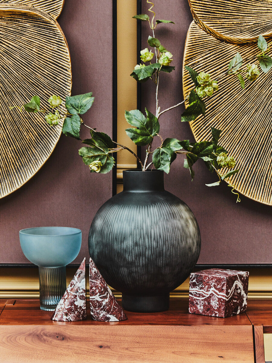 Dark gray ribbed ceramic vase with rounded body and narrow neck paired with small light blue glass vase