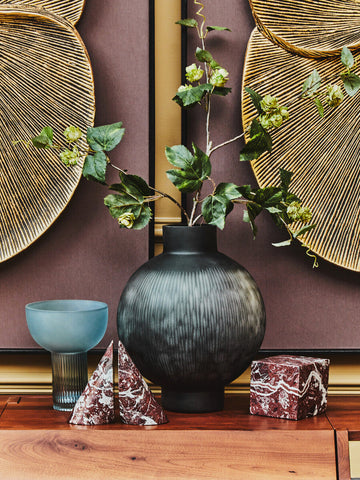 Dark gray ribbed ceramic vase with rounded body and narrow neck paired with small light blue glass vase