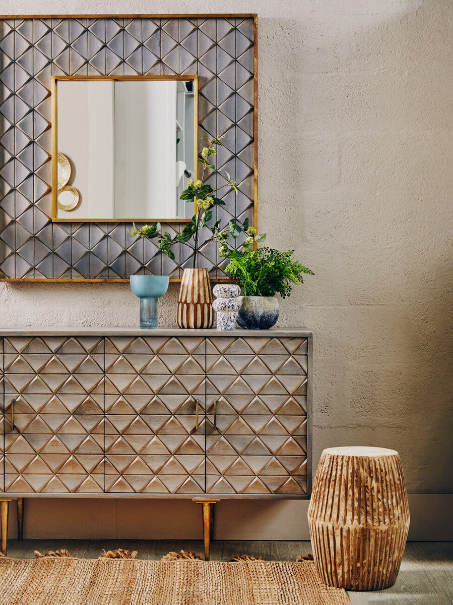 Gold-framed rectangular mirror with geometric diamond-patterned metallic backing next to a small light blue glass vase