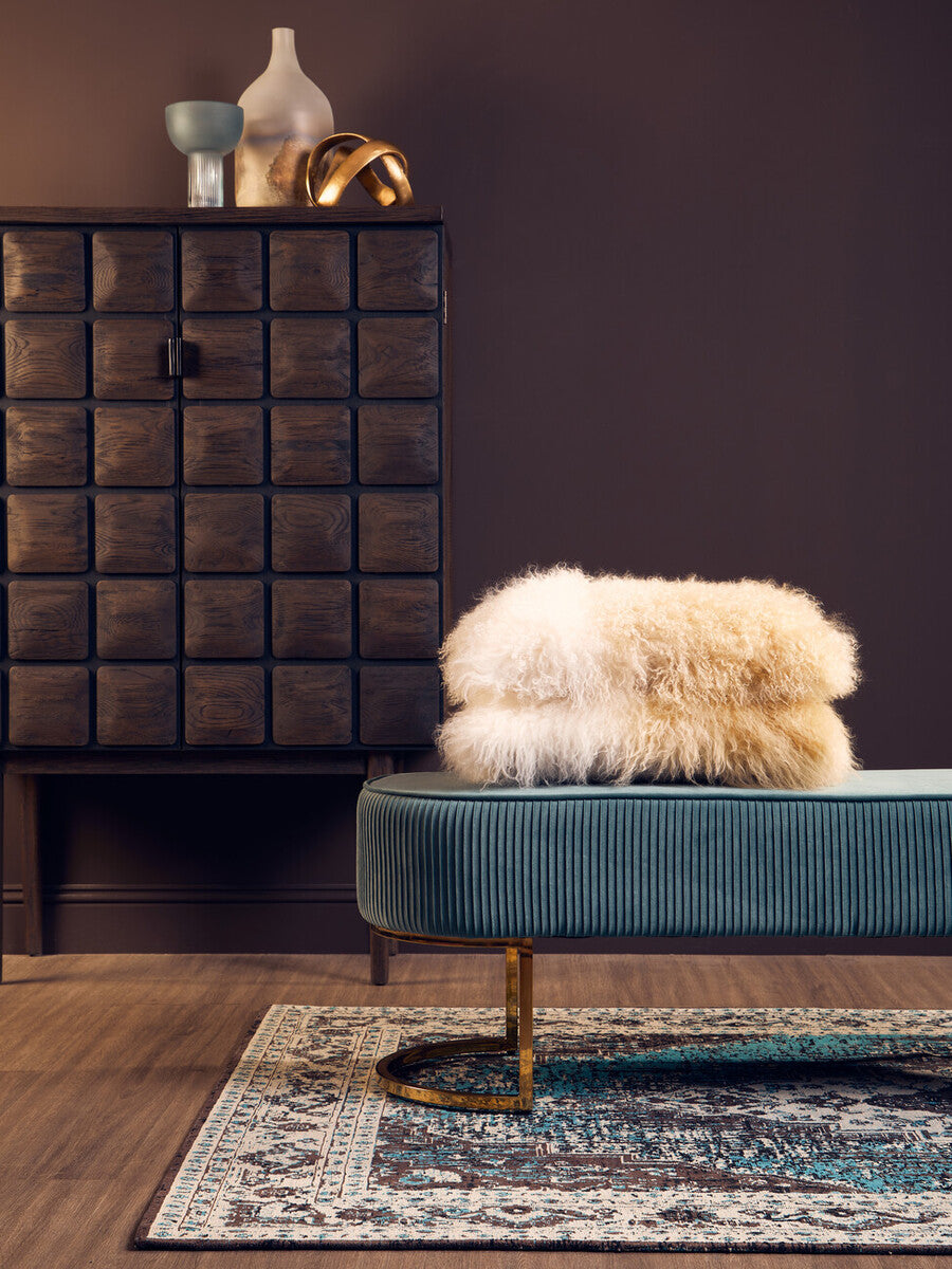 Teal velvet bench with gold-tone curved legs and a fluffy cream sheepskin throw holding a small light blue glass vase