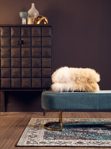Teal velvet bench with gold-tone curved legs and a fluffy cream sheepskin throw holding a small light blue glass vase