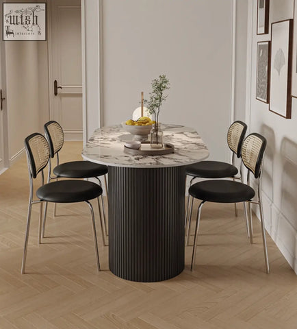 Modern esther oval dining table with white marble top and black ribbed base, surrounded by cane back chairs with leather seats