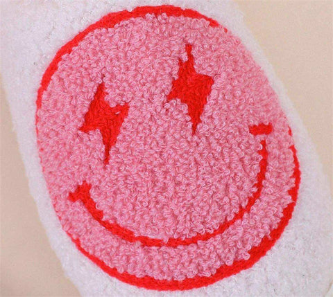 Pink fuzzy smiley face patch with red lightning bolts on white fabric of euphoria slippers to help you stay warm