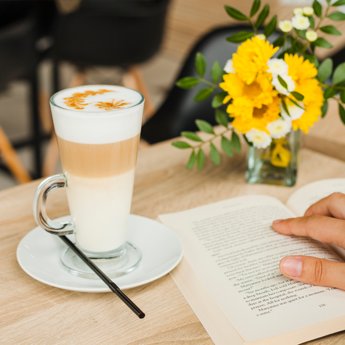 A tall clear glass latte with layered milk and coffee topped with an orange flower design in euri latte glasses set of 4