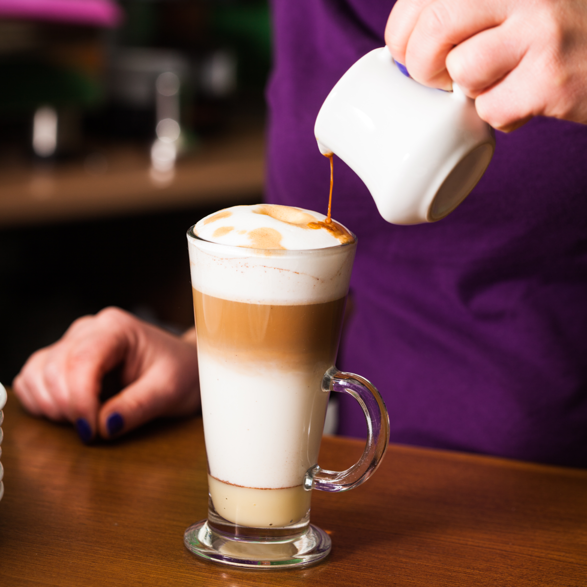 A tall clear glass latte glass from the euri latte glasses set holds creamy milk foam over rich brown coffee