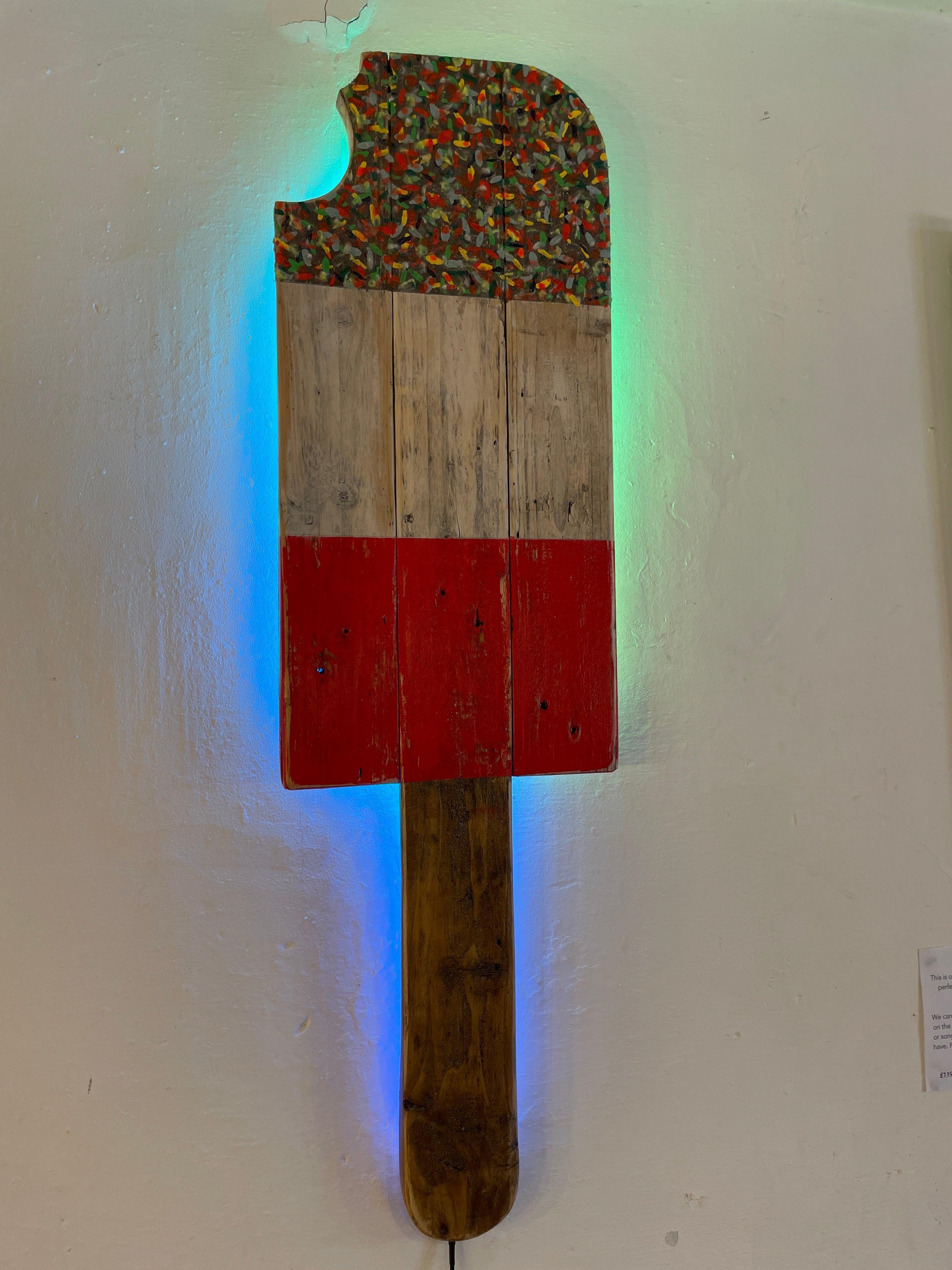 Rustic wooden fab lolly wall light with colourful textured top and red base featuring colour changing led glow