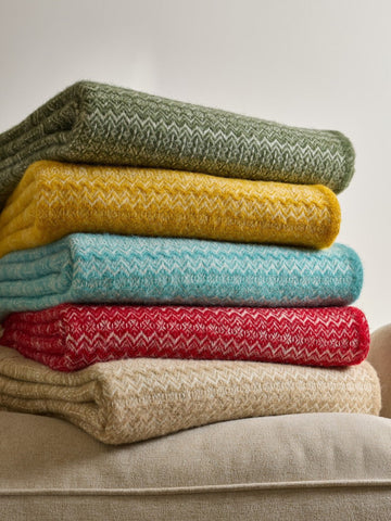 Stack of five fair isle pure new wool throw blankets in olive, mustard, teal, red with white pattern, and beige colors