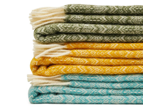 Stack of fair isle pure new wool throws in olive green mustard yellow and teal blue with cream-colored fringe