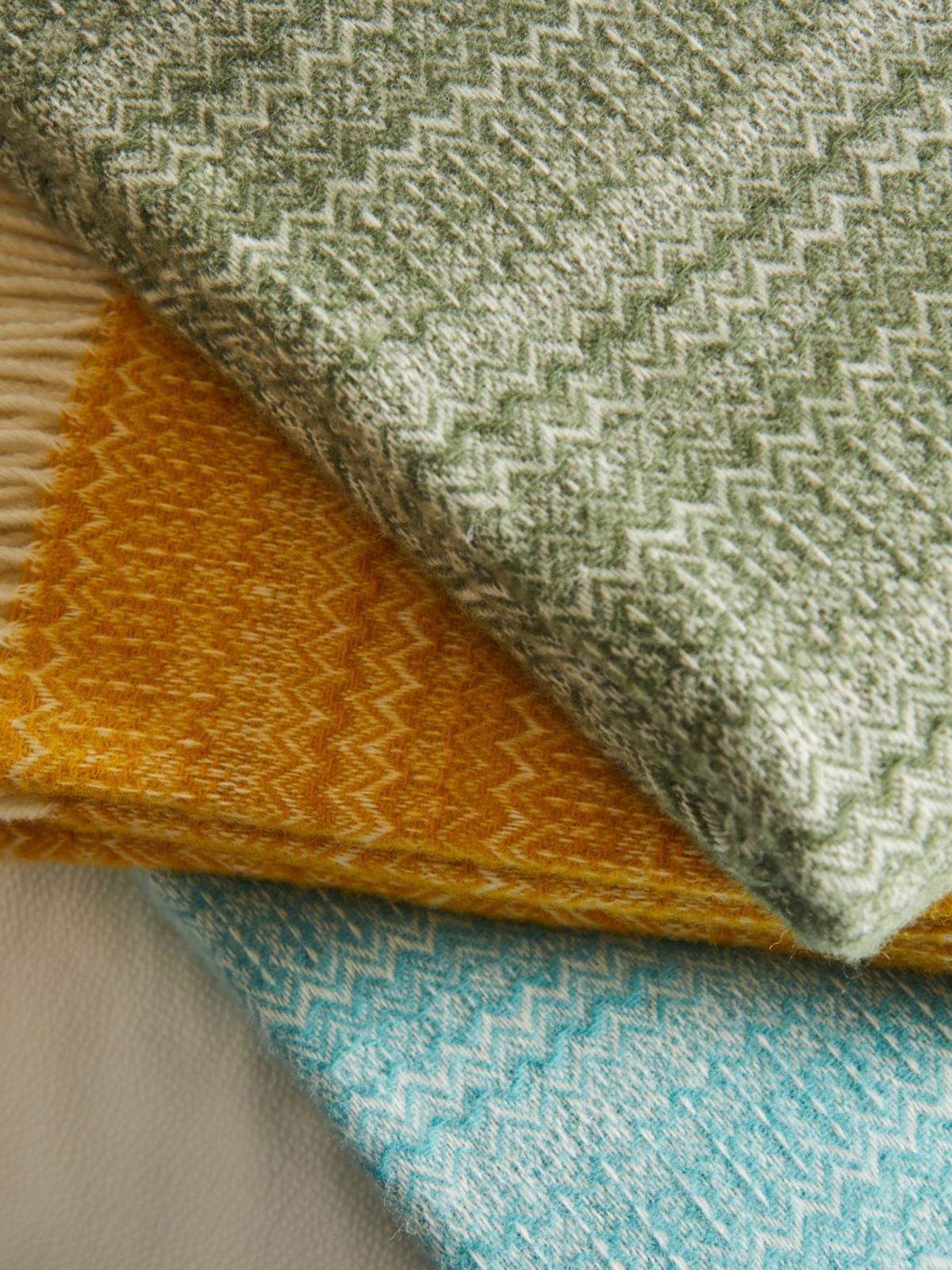 Stacked fair isle pure new wool throw blankets in olive green mustard yellow and teal with a textured zigzag pattern