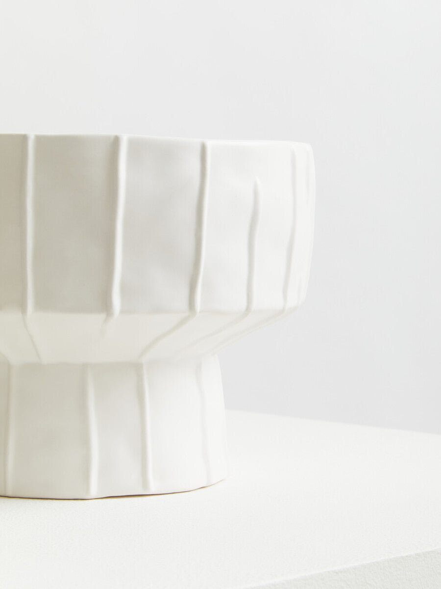 A sleek white ceramic fara white vase with a fluted geometric design and sturdy pedestal base