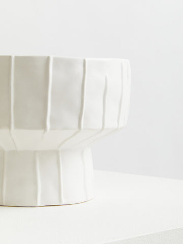 A sleek white ceramic fara white vase with a fluted geometric design and sturdy pedestal base