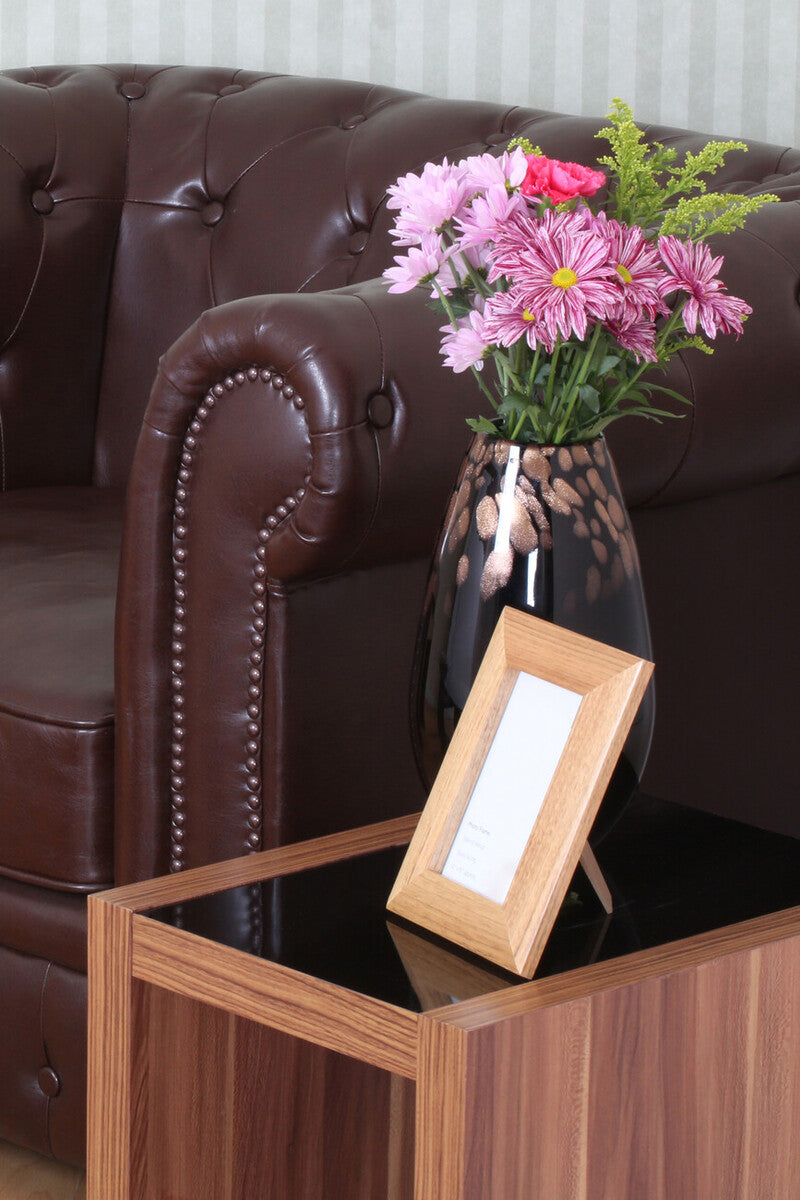 Black ceramic vase with gold leaf pattern holding pink and red flowers on walnut veneer fargo nest of three tables