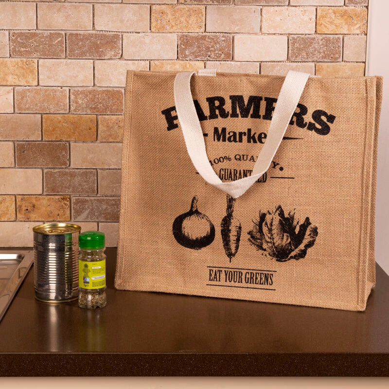 Beige jute farmers market shopping bag with white handles and black vegetable print eat your greens design