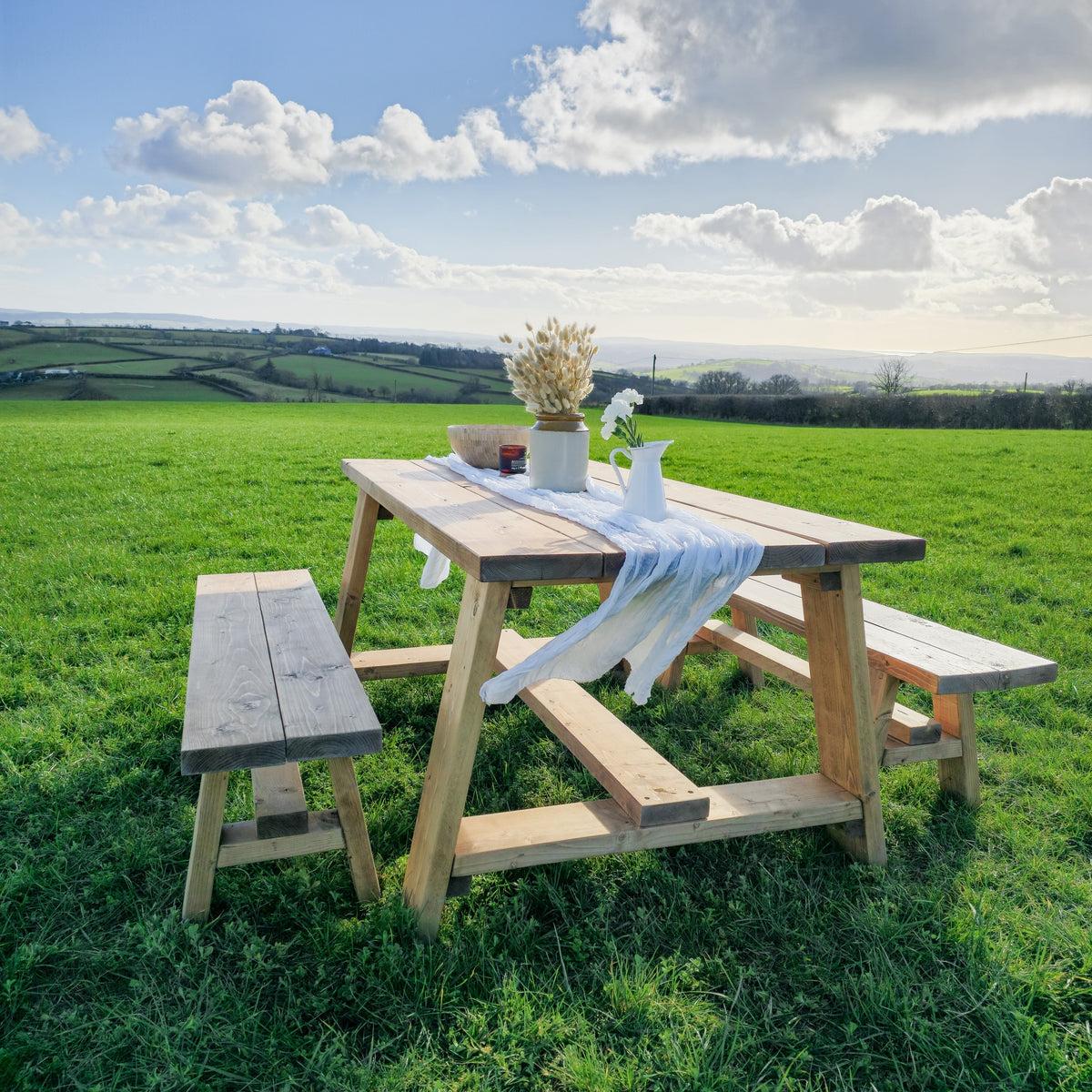 Rustic farmhouse outdoor table with timber legs and attached benches in light natural wood finish with white cloth