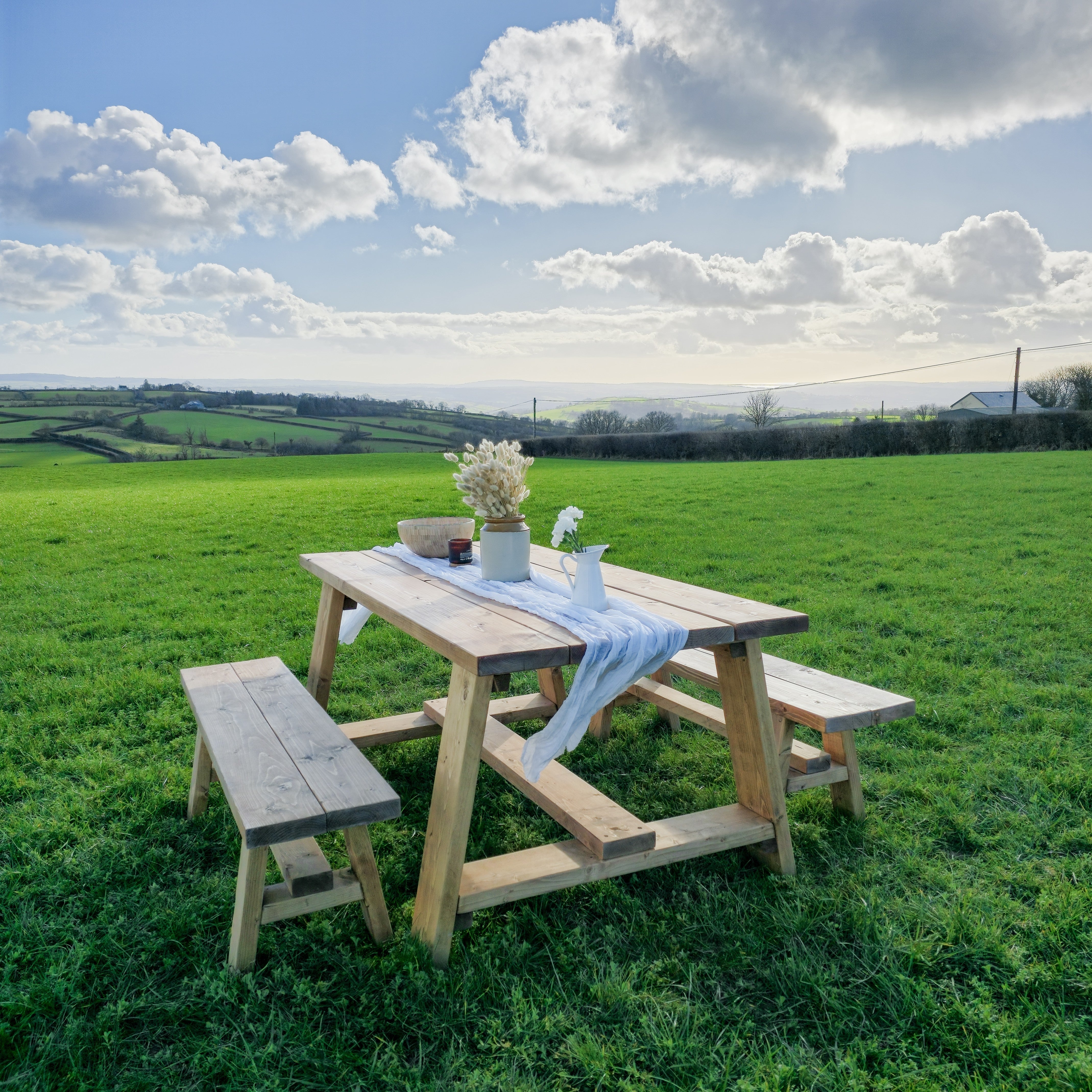 Rustic farmhouse outdoor table with timber legs and attached benches in light natural wood finish and simple construction