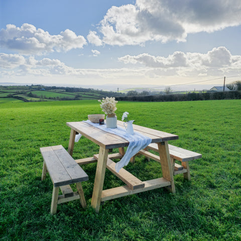 Rustic farmhouse outdoor table with timber legs and attached benches in light natural wood finish and simple construction