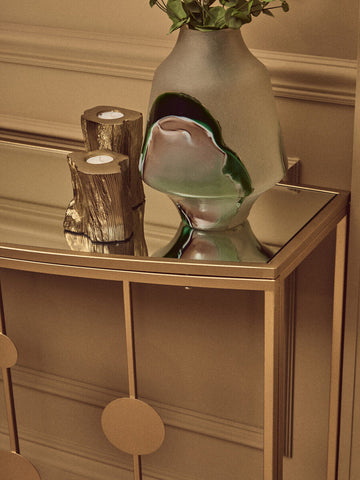A translucent frosted glass vase with green and gray swirls on a farran champagne gold finish console table with mirror top