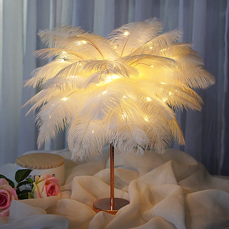 A glowing white feather lamp with warm led lights on a rose gold stand ideal for bedroom decoration with remote control and power supply